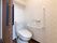 居室に設置されたトイレ。洋式の水洗トイレで、壁には手すりとナースコールがついている。後方の頭上には収納棚がある。