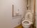 白い壁で清潔感のある広いトイレになっている。壁に手すりをL字型に取り付けており、立ち上がる時に体を支えることができる。
