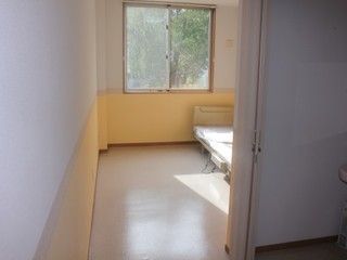 突き当りが窓になっており、室内は明るい雰囲気。低床型のベッドが壁に寄せて置かれており、手前には洗面台がある。
