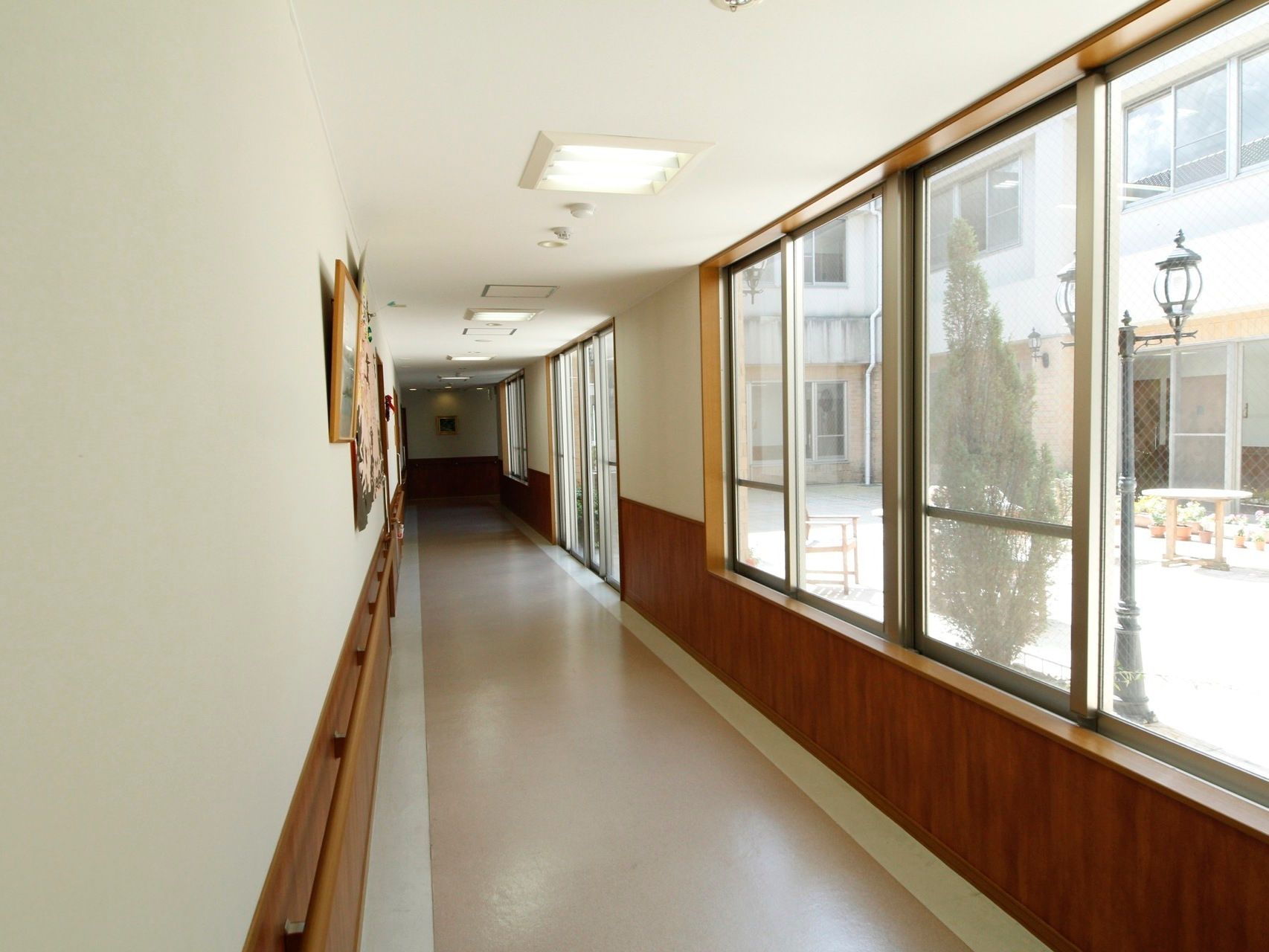 白い壁に茶色の腰板のついた廊下である。右側は中庭で、大きな窓や、中庭に出られる掃き出し窓となっている。