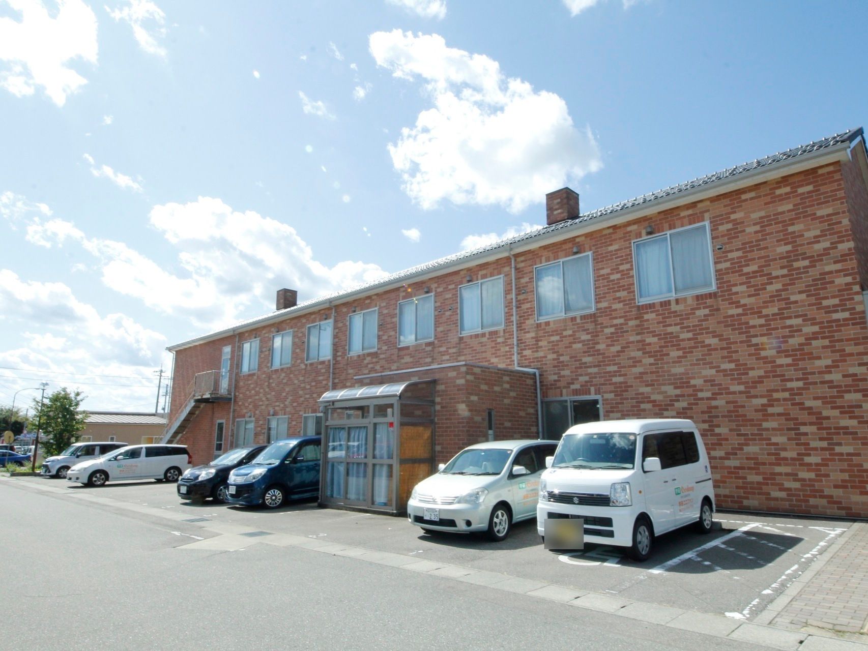 オレンジ系のモザイクレンガが印象的な外観の、２階建ての建物である。壁に沿って、駐車スペースが取られている。