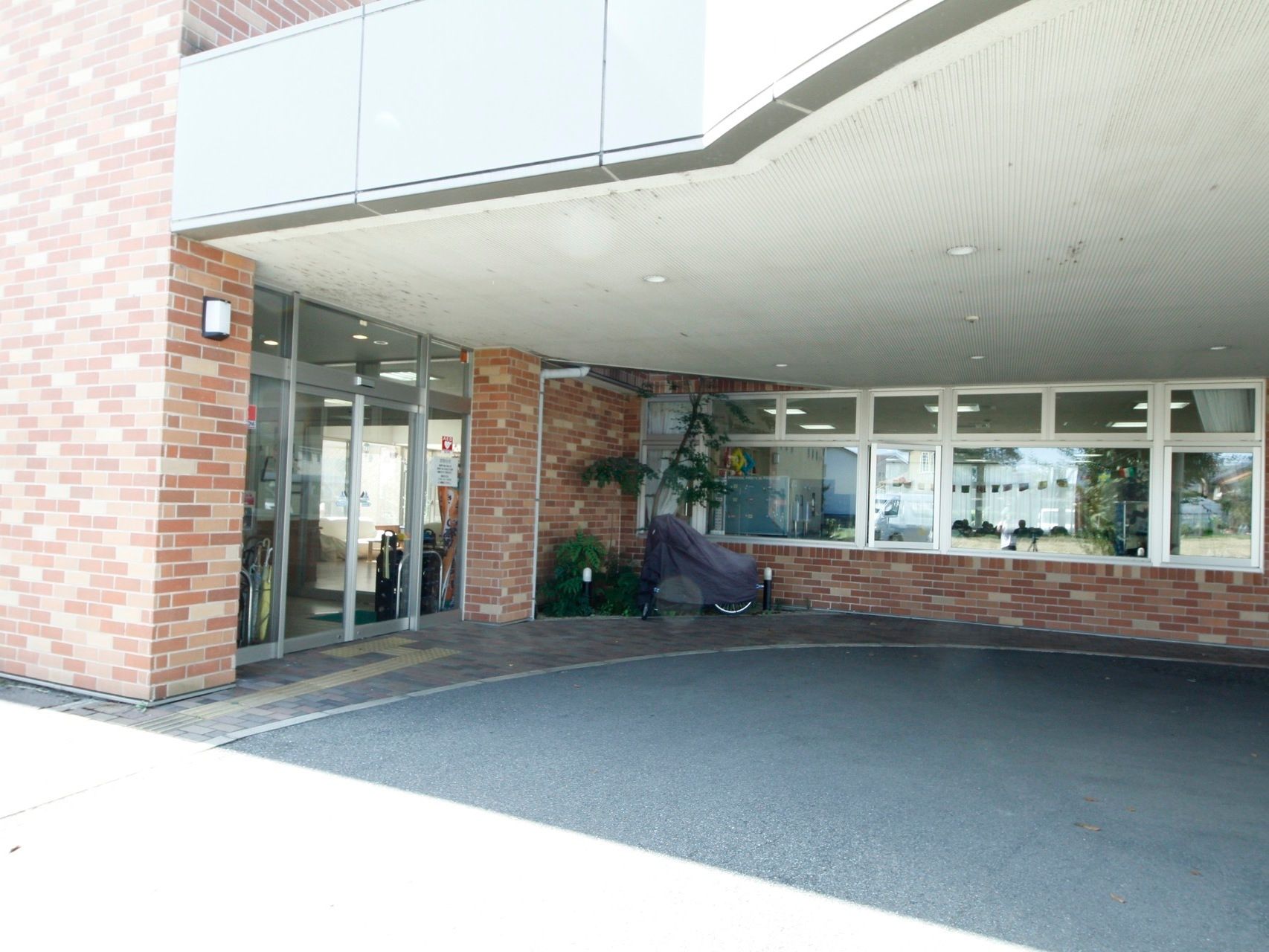 透明の自動ドアの入り口である。入り口前には屋根があり、車で屋根の下まで入ることができる。周りの壁はレンガである。