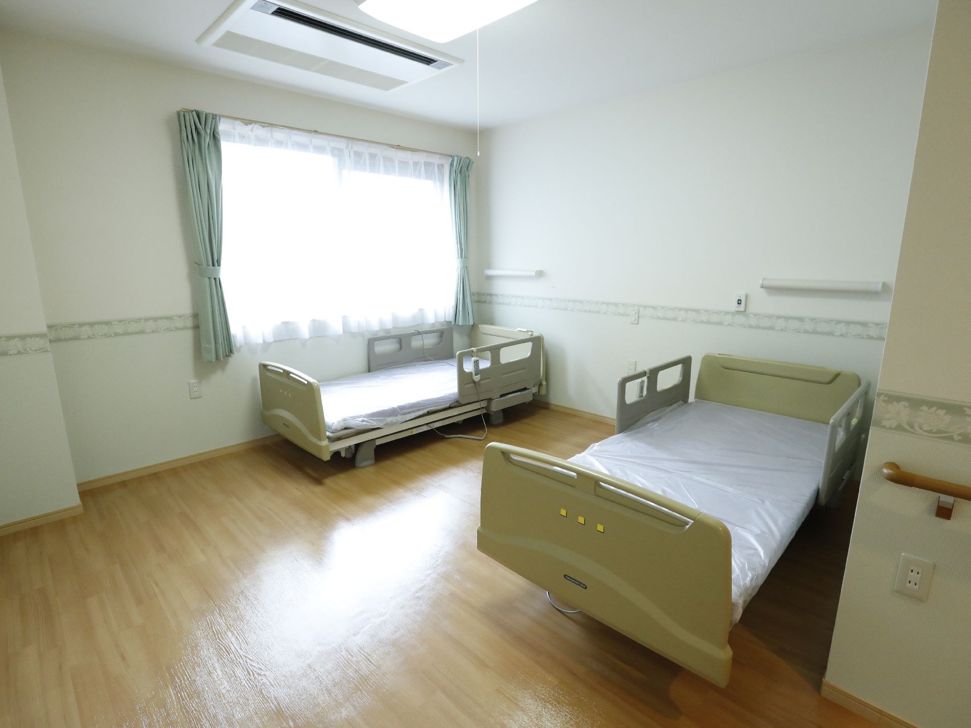 ワンルームのフローリングの室内には、エアコンが完備してある。室内にはベッドが二台置いてある。窓にはレースと布のカーテンが取り付けてある。