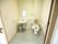 洋式トイレがある。手を洗う場所が設けてある。壁に鏡がついている。シングルレバーの蛇口である。仕切るための蛇腹カーテンがある。