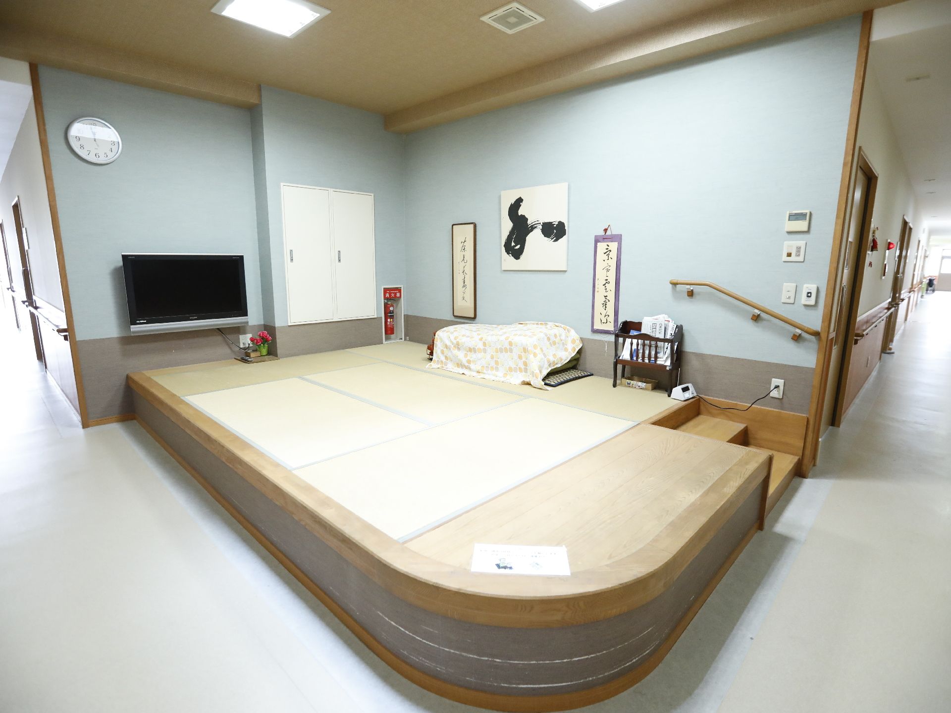 和室がある。消火器が置いてある。テレビが置いてある。掛け軸がかけてある。手すりがついた階段があり、楽に和室に入ることができる。