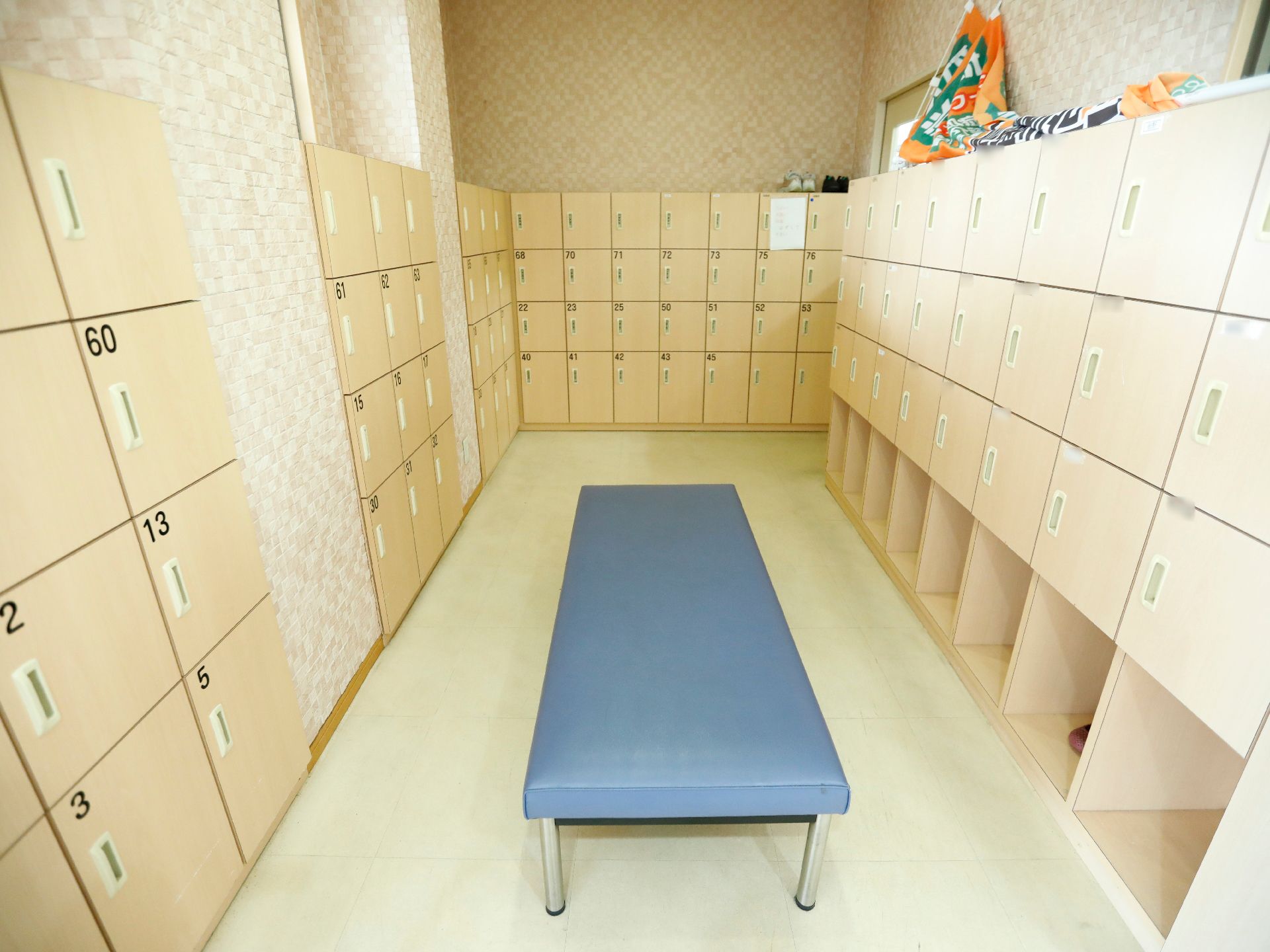 周囲の壁の前には扉の付いた大型の靴箱が複数設置されている。扉の左上には名前や番号が貼られている。中央にはベンチが置かれている。
