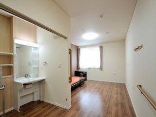 広々とした居室には、足元が当たらないデザインの洗面台を備えている。正面の横側に窓があり、出入口傍の壁に手すりを設置している。