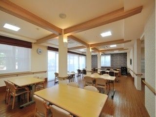 広々としたリビングには、テーブルセットを間隔を置いて並べている。天井が高く開放感に溢れている。横側にガラス張りが広がり明るい空間である。