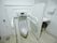男性用トイレが設置してある。センサーで水が流れるつくりである。手すりが設けてある。緊急用ブザーがある。衝立があり、洗面所が見える。