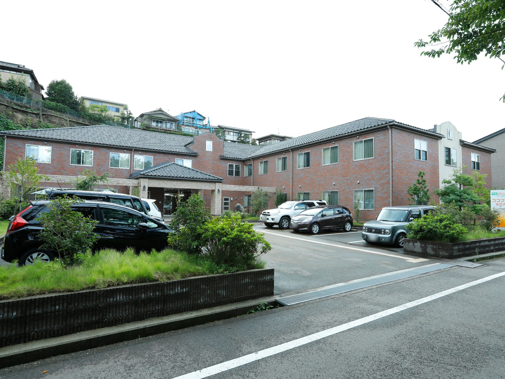 道路と敷地の間に花壇があり、駐車場、2階建ての赤レンガ風の建物がある施設