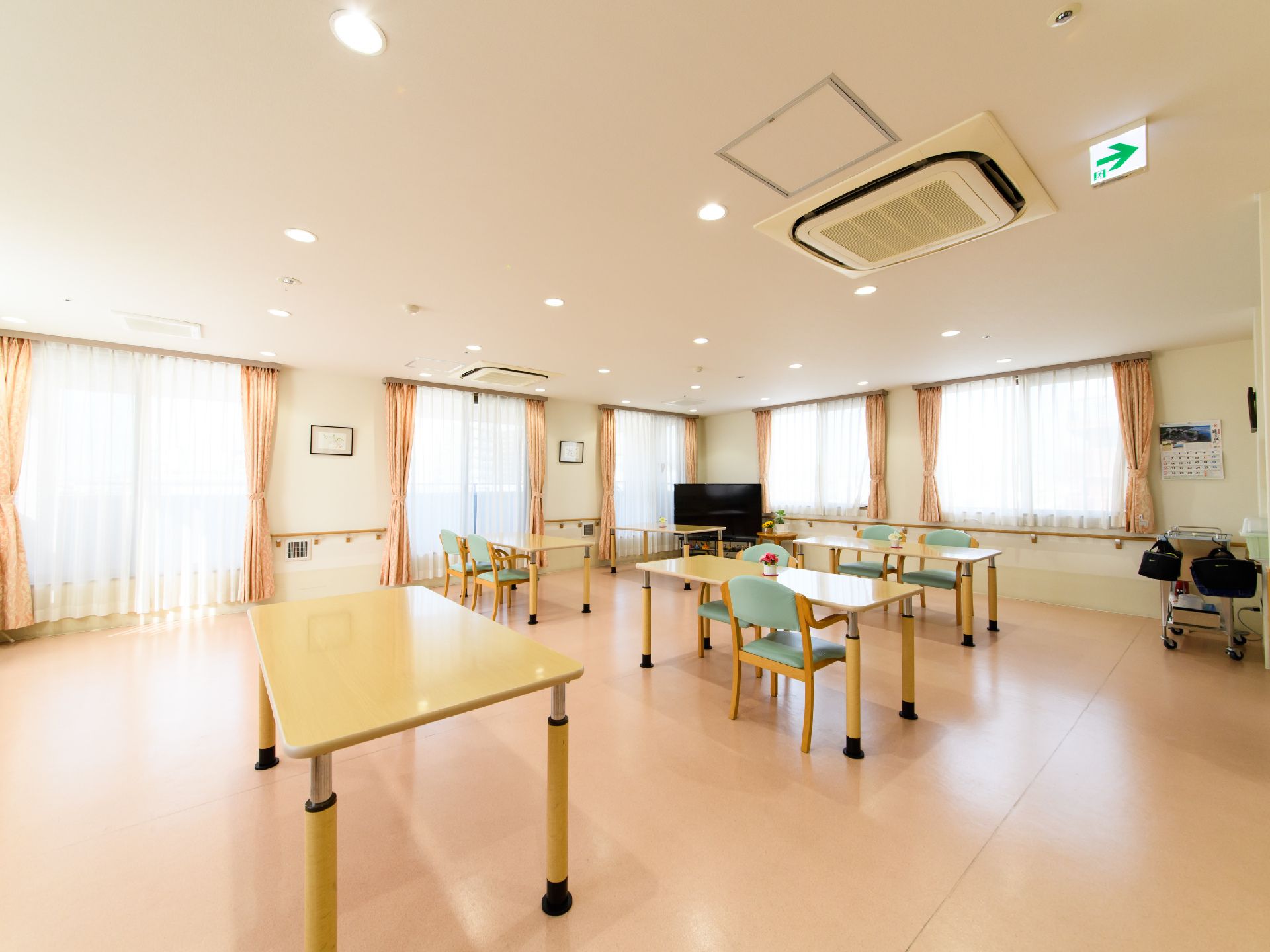 白色の天井と壁にベージュ色の床の内装である。テーブルとグリーン色の椅子が並べてあり、角にはテレビが置いてある。