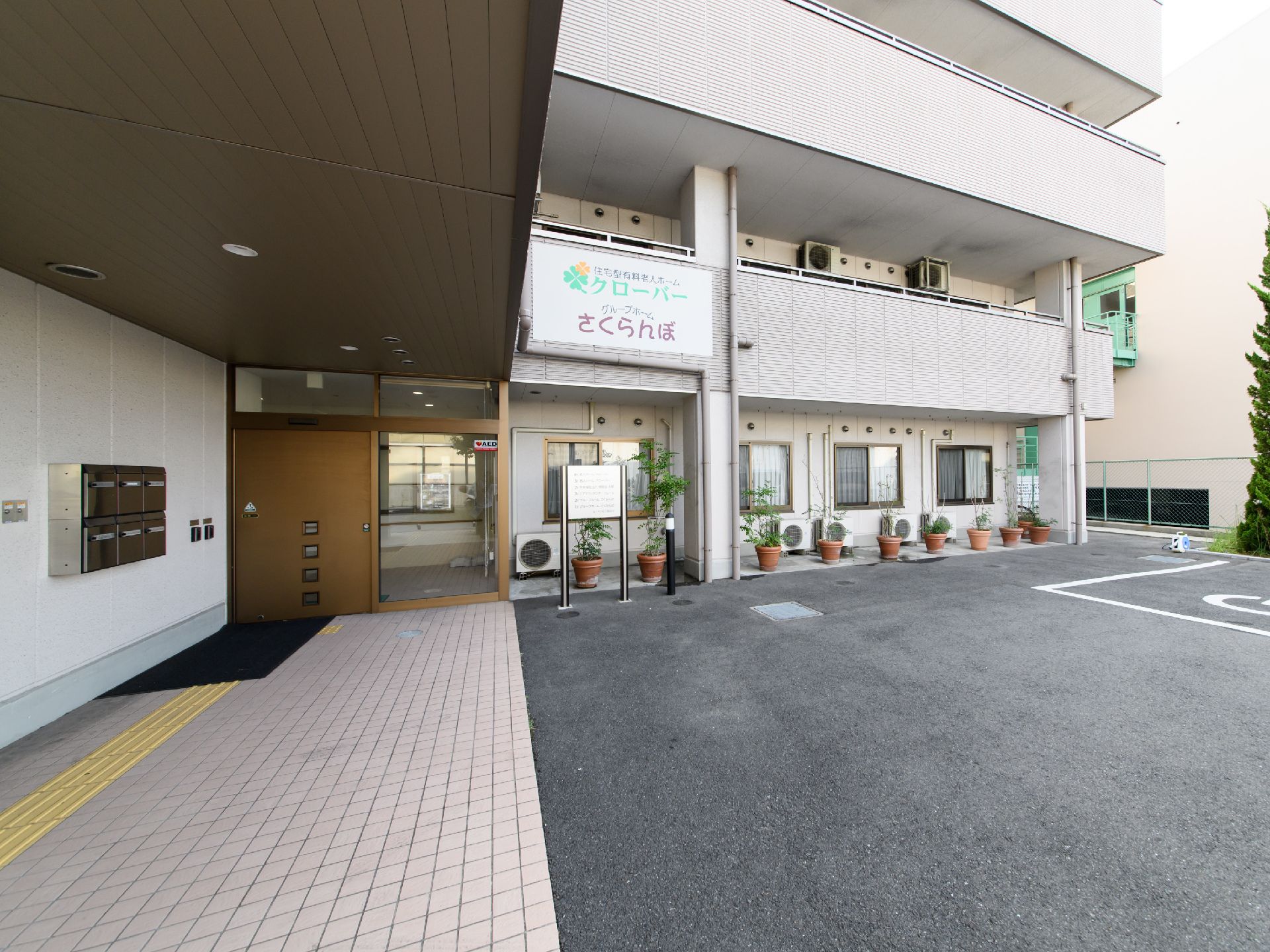建物の前駐車場になっている。入口までのアプローチは歩道部分はタイル敷きになっていて、屋根が付いている。