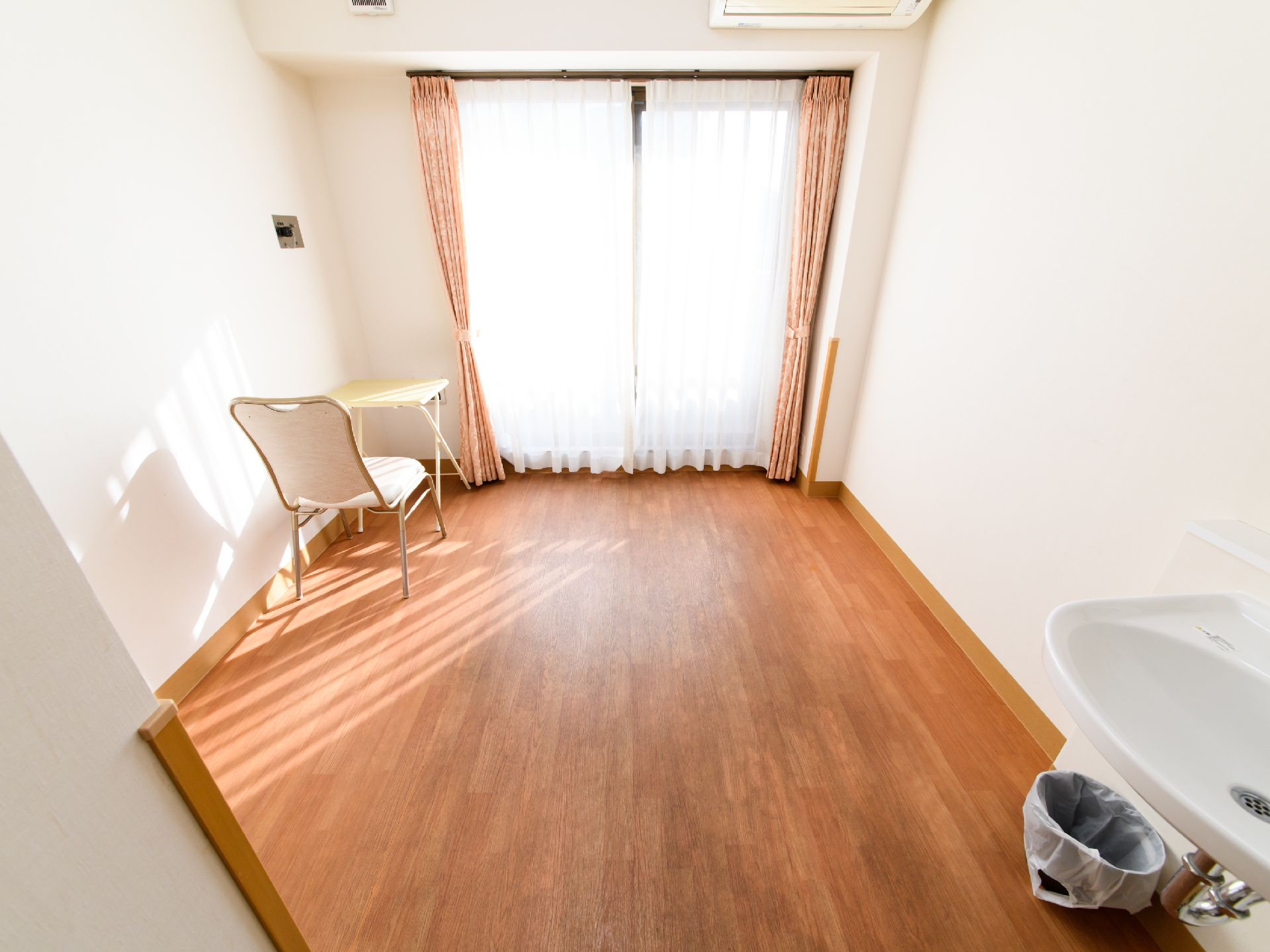 居室の壁は白、床は落ち着いた色のフローリングになっている。大きな窓からはたっぷりと陽が差し込んでいる。