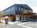 広い通りに面した歩道の脇に駐車場への案内看板がある。建物の側面には屋根と木製フェンスの設置されたスペースがある。