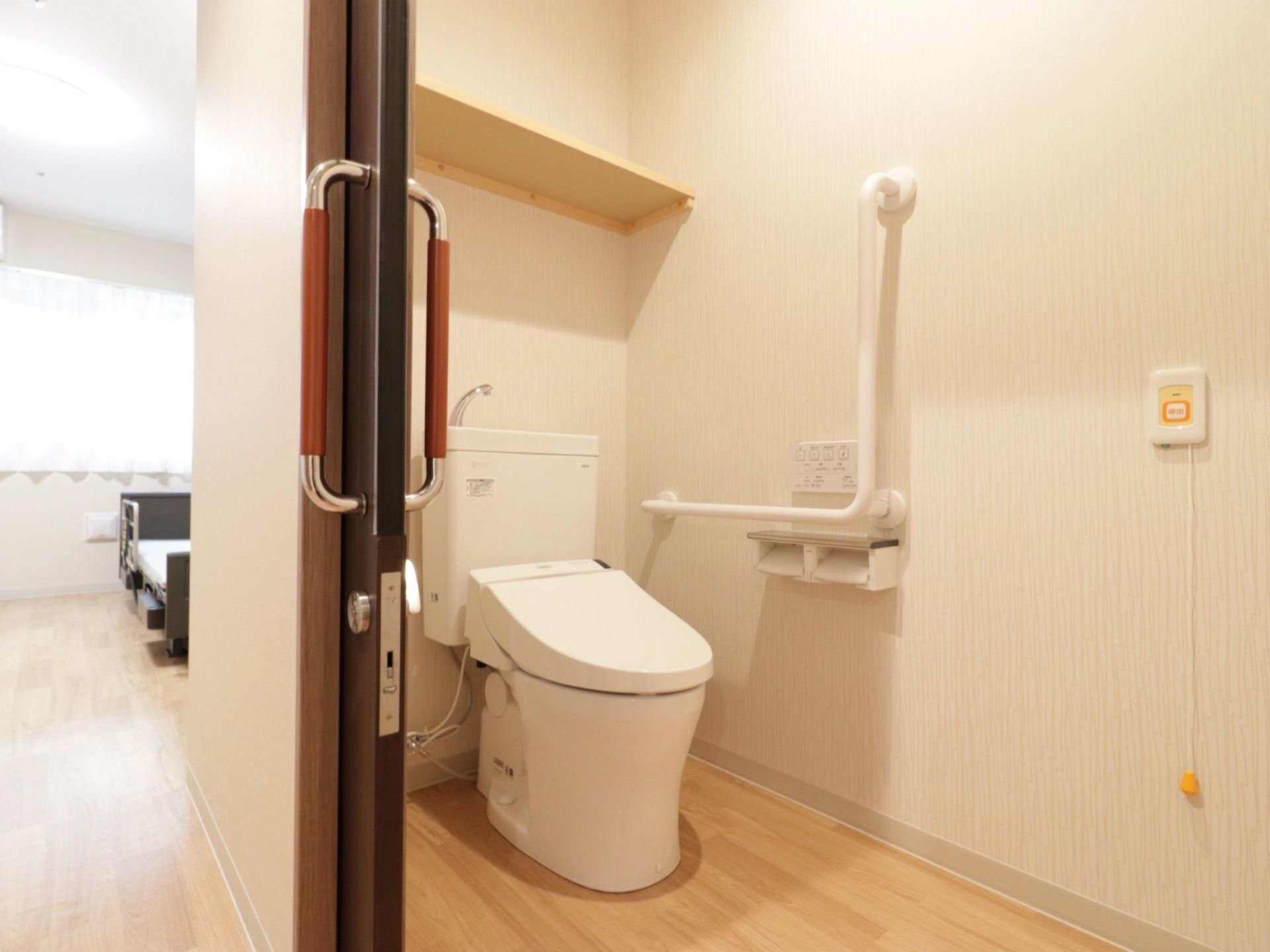 洋式のトイレである。壁面にはL字型の手すりが取り付けられており、緊急時の呼び出しベルも備わっている。