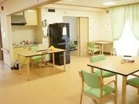 リビングには木調のテーブルと手すり付きの椅子が置かれている。カーテンの付いた大きな窓から光が差し込み、室内は明るい雰囲気である。