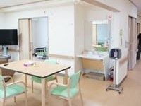 リビングにはテーブルと手すり付きの椅子、テレビ、洗面台が設置されている。壁の色は白色系であり、室内は明るい雰囲気である。