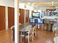 木調のテーブル、手すり付きの椅子が置かれ、テレビが設置されている。床と壁、家具の色は統一され落ち着いた感じである。