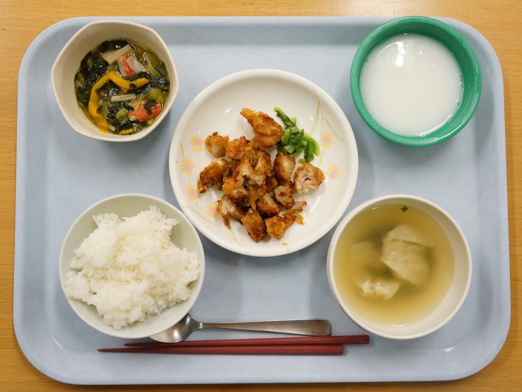 ご飯とワンタンスープ、野菜の入った小鉢と鶏のから揚げ、デザートがお盆に並べられている。お箸とスプーンもある。