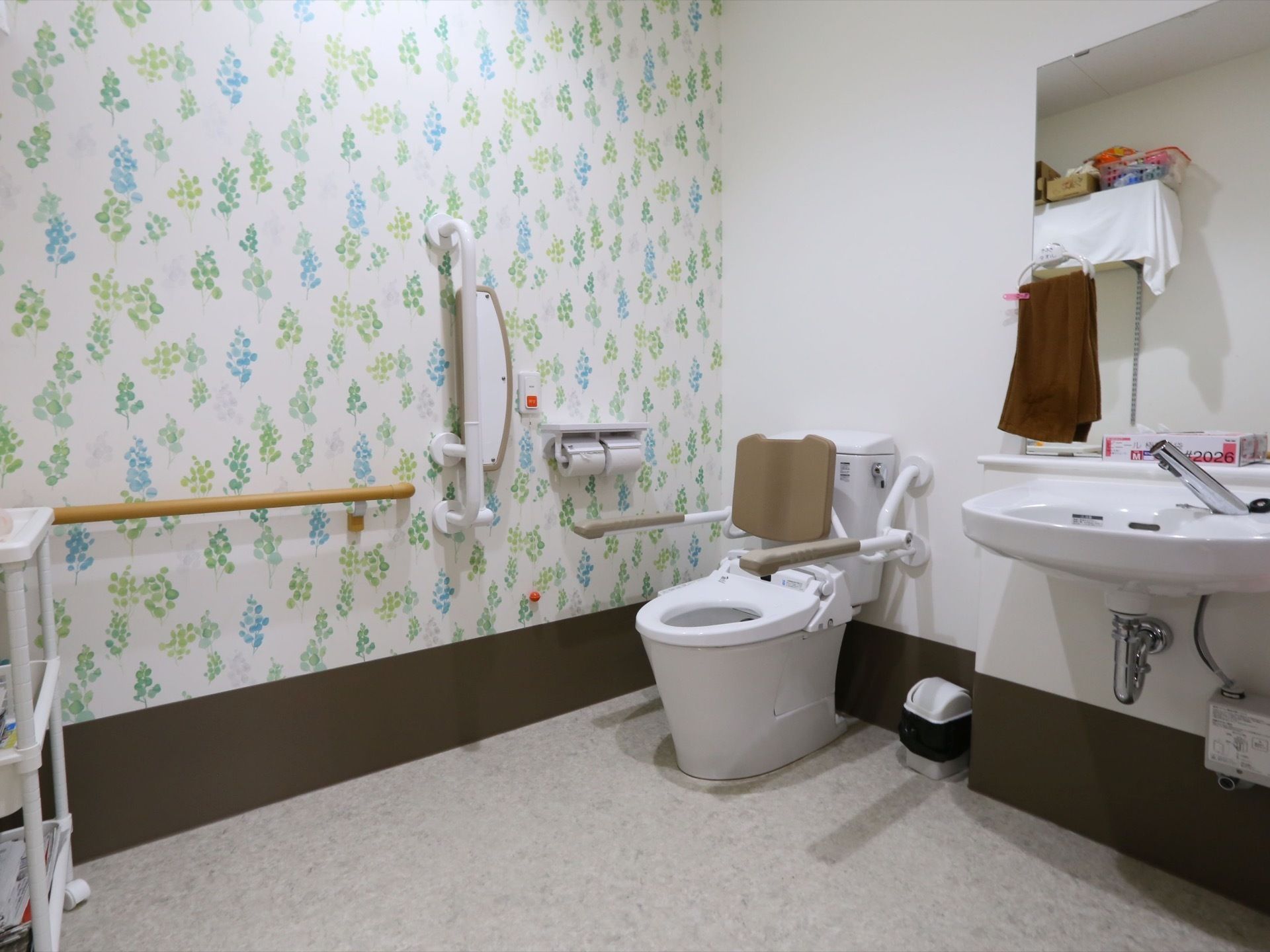ナースコールや手すりが取りつけられた、バリアフリー仕様のトイレである。横にはフットレスタイプの洗面台が設置されている。