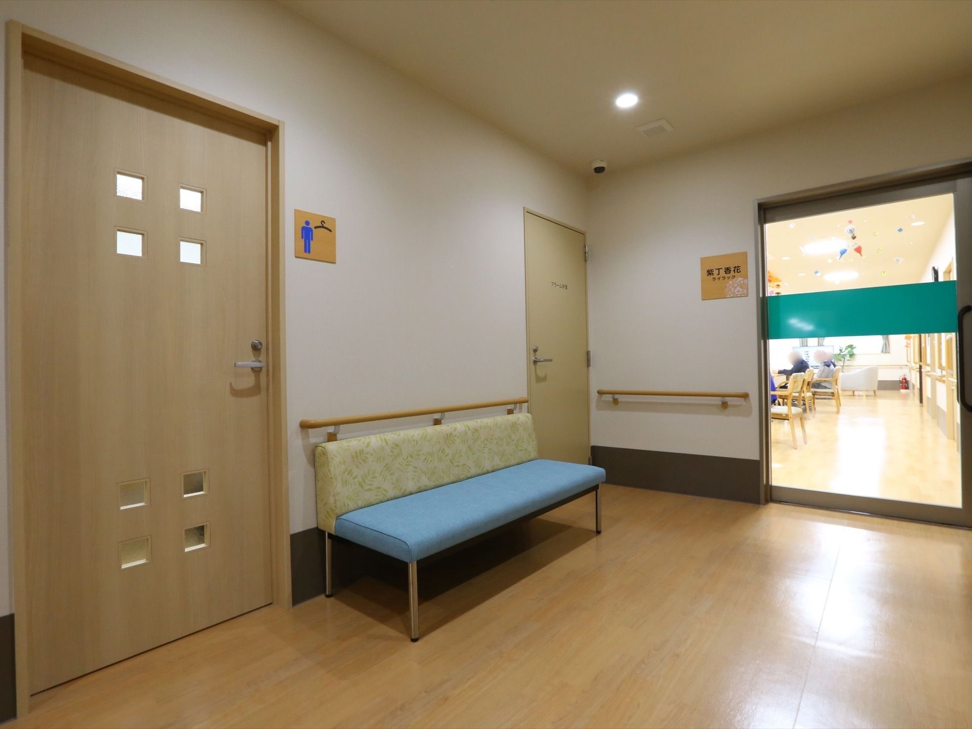 男性トイレのドア横にベンチが置かれた通路、リビングの入り口のガラスの扉