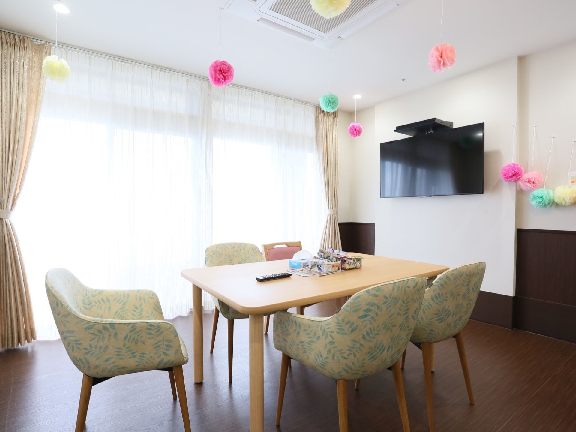 テーブルと椅子が置いてあり、壁に薄型テレビが設置されている。天井からカラフルなお手製の飾りが吊るされている。