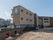 中央に施設が建っている。施設の一階部分、右側には黒色のフェンスがある。フェンスは途中からレンガ塀に変わっている。