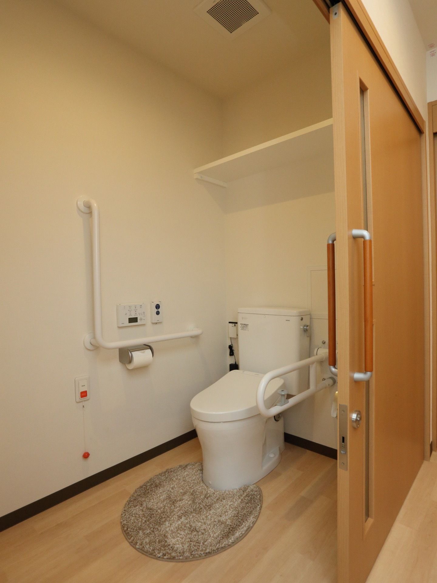 トイレの扉は引き戸式で、開口部が広々としている。可動式の手すりも完備している。壁の下部には、ナースコールが取りつけられている。