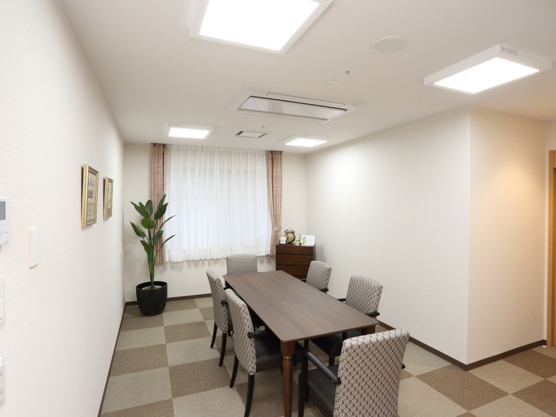 グレーの格子柄のクッションフロアが敷かれた部屋である。窓のそばに観葉植物が置かれている。空調機が完備されている。