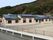 広い面積を有した、１階建ての落ち着いた色合いのグループホームである。手前の道路には、ガードレールが設置されている。