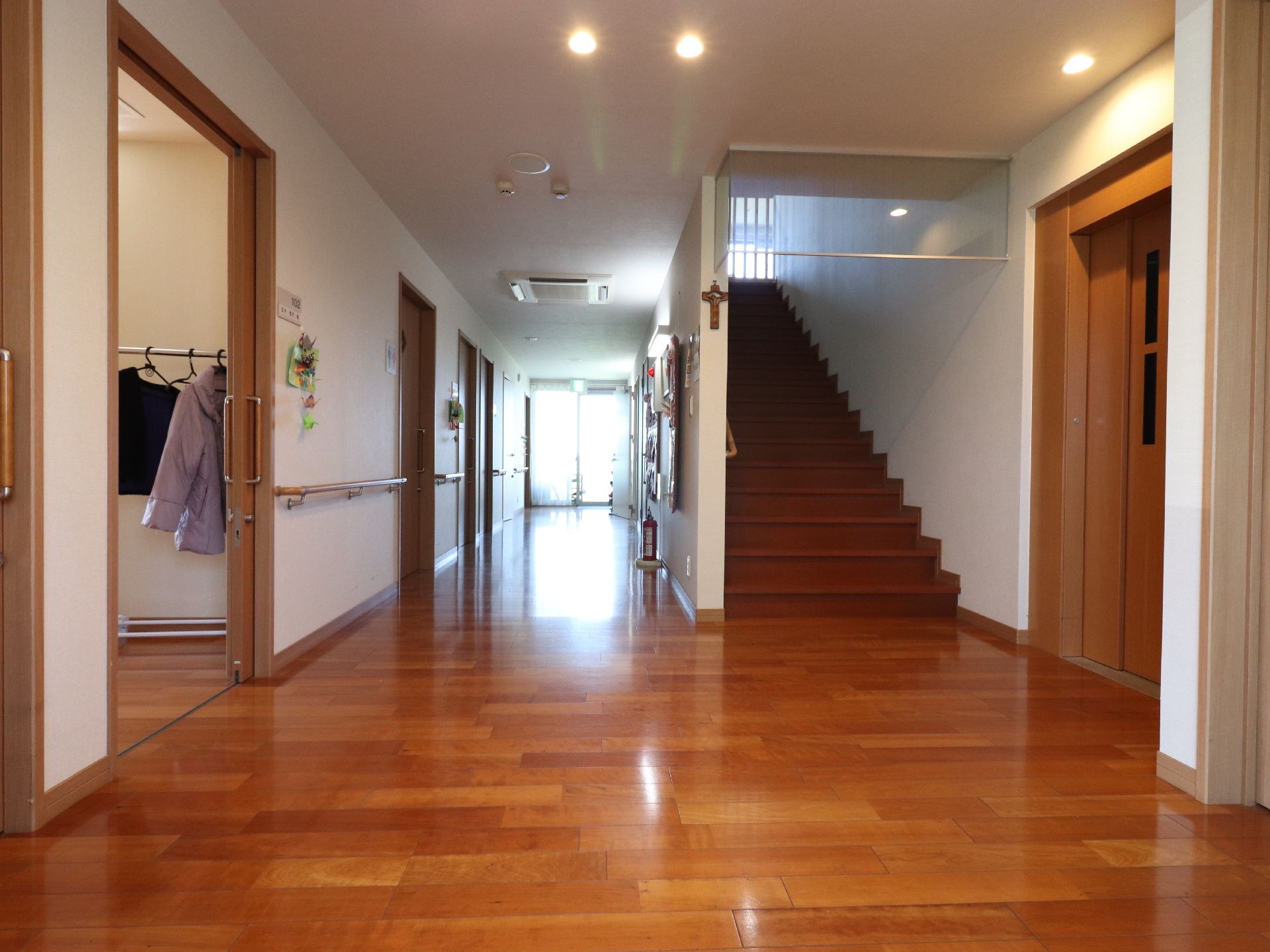 エレベーター前の廊下は広々としており、入居者様の居室ドアへとつながっている。エレベーターを使用しない場合は、階段も利用できる。