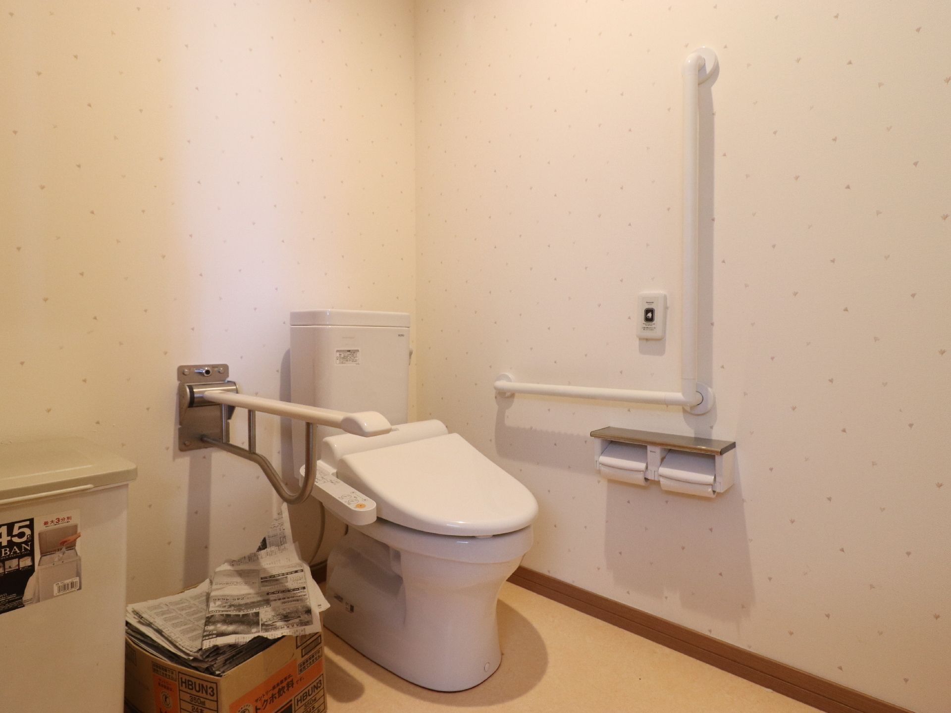 トイレの壁は白く、床はフローリングで掃除がしやすくなっている。段ボールに新聞紙がたくさん入れてあり、ごみ箱も設置されている。
