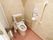 トイレの洋式便器には背もたれとひじ掛けが付けられている。壁側には縦長の手すりと呼び出しボタンがある。