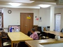 ダイニングテーブルと肘掛け椅子が並べられた食堂。テレビがあるのでゆったりお過ごしいただける。白い壁には手すりが取り付けられている。