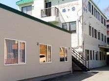 白い外壁と緑の屋根の３階建ての建物があり、その横に平屋の建物が並んでいる。３階建ての建物の壁に施設の名前が掲げられている。