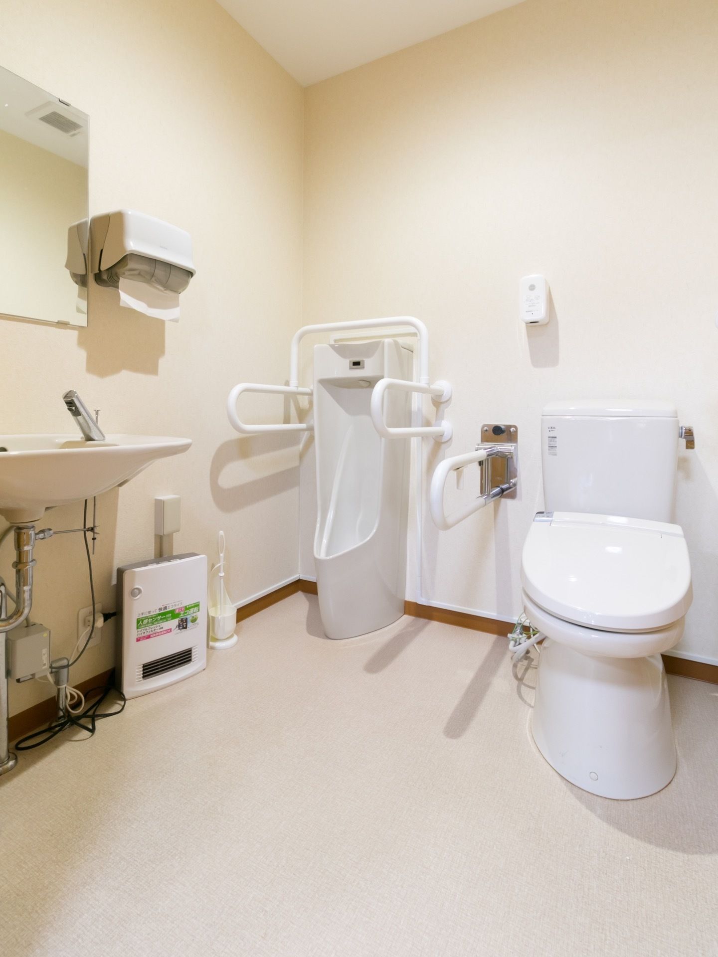 共用トイレには手すりのついた洋式便器のほか、男性用の小便器もある。手前に手洗い器があり、鏡やペーパータオルも備えつけられている。