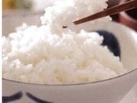 藍色の模様が入った白色の茶碗に、ご飯が多く盛り付けられている。茶色のお箸で一口分が持ち上げられている。