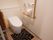 床にはトイレマットが敷かれている。温水洗浄便座トイレを採用しており、壁にはＬ字型の手すりが備わっている。