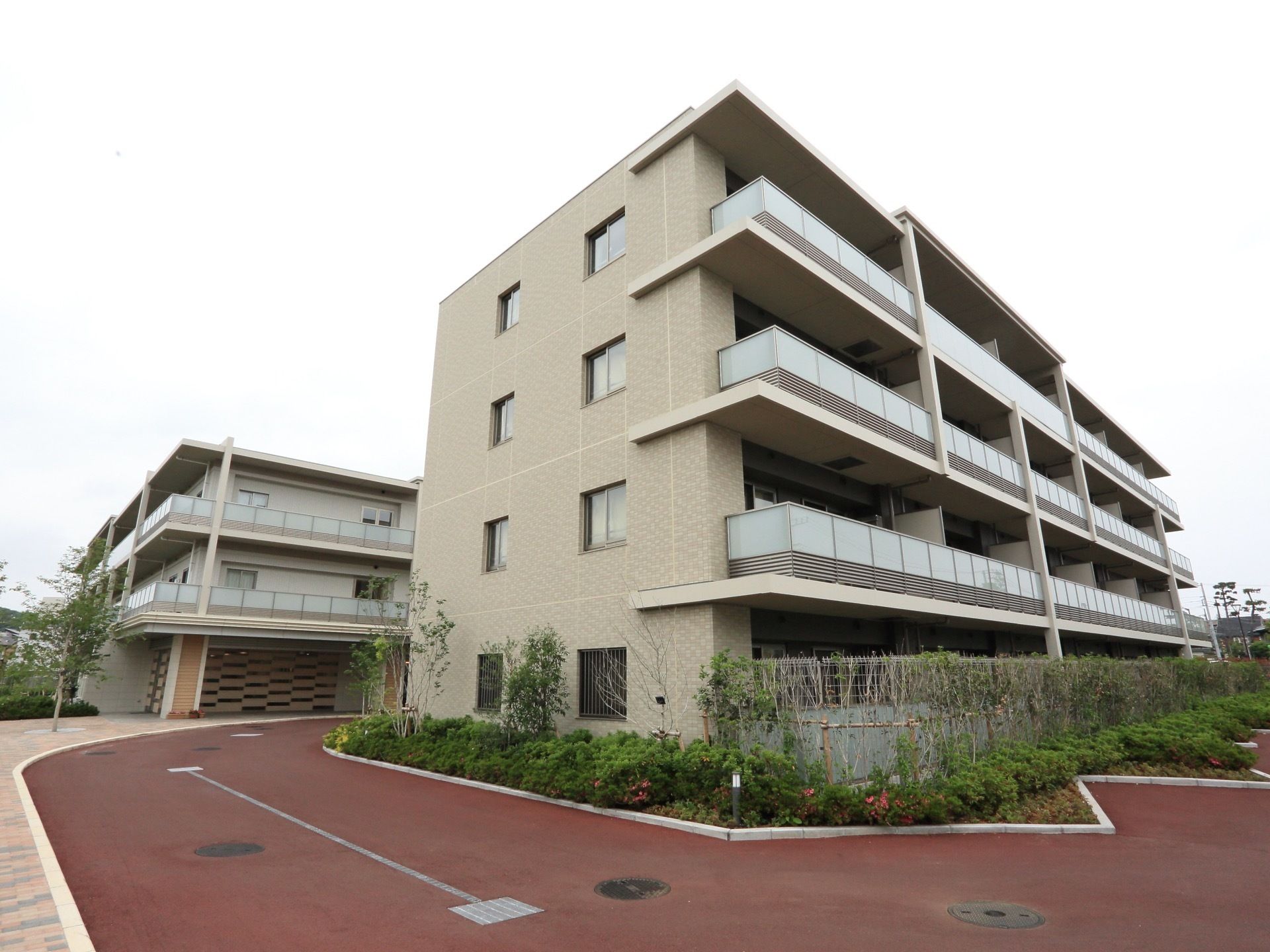 建物は４階建てで淡いベージュの外壁である。建物の周りには綺麗に手入れをされた木や花が植えられている。