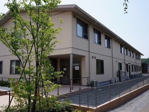 手前に植栽があり周囲がフェンスで囲まれている、二階建ての建物