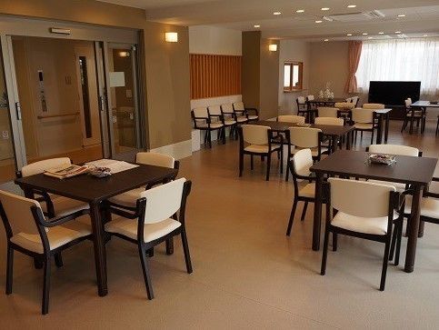 優しい色の照明が取り付けられているテーブルと椅子が並んでいる食堂