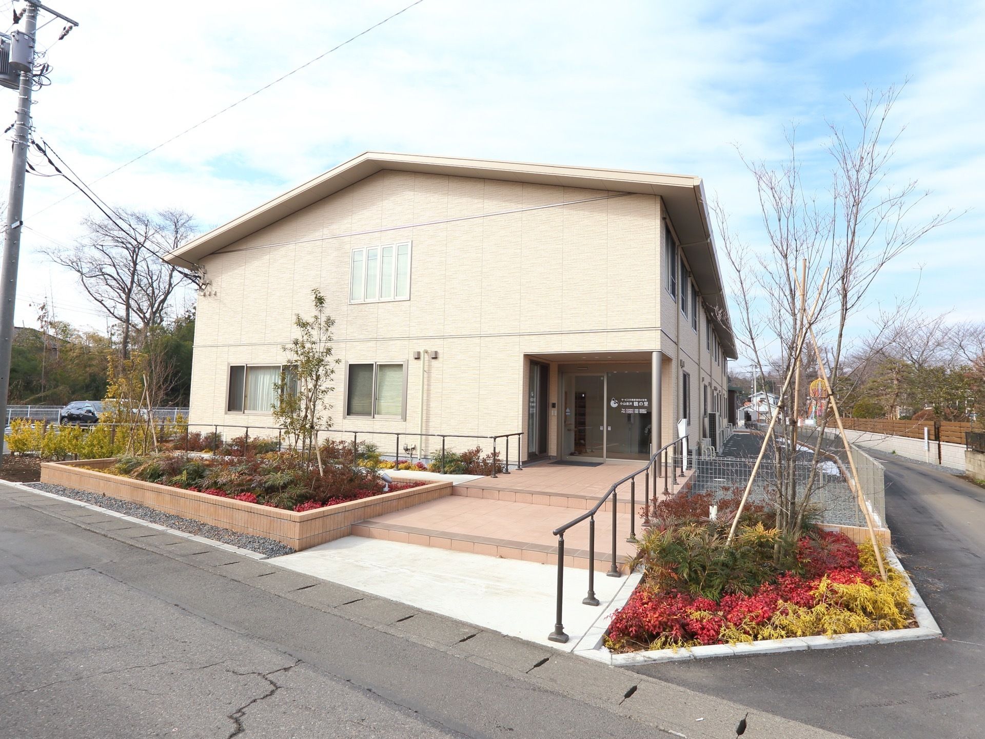淡いベージュ色の施設の建物である。手前は階段で左側はスロープが設置されており、それぞれの通路で出入口に向うことができる。