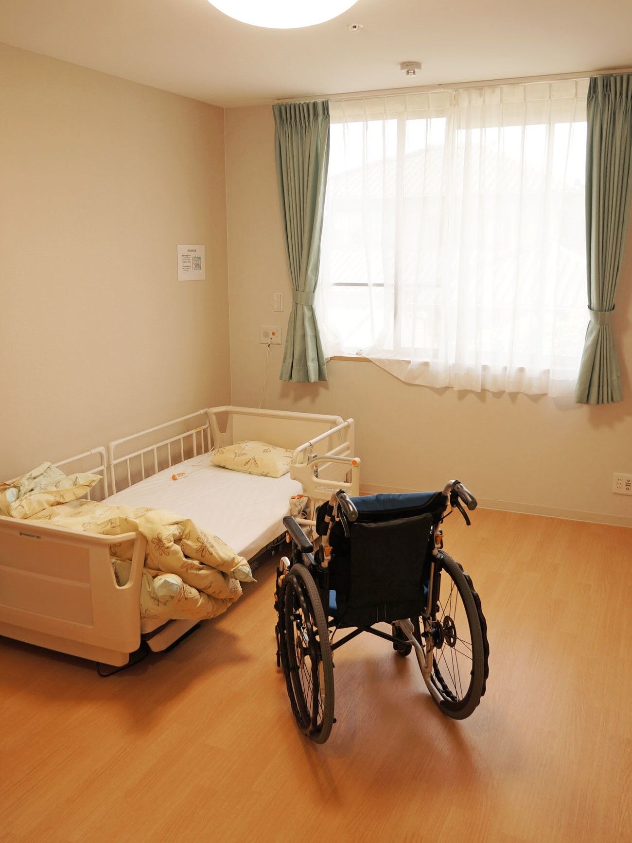 ベッドと、部屋の中央に車椅子が置いてあるフローリングの居室