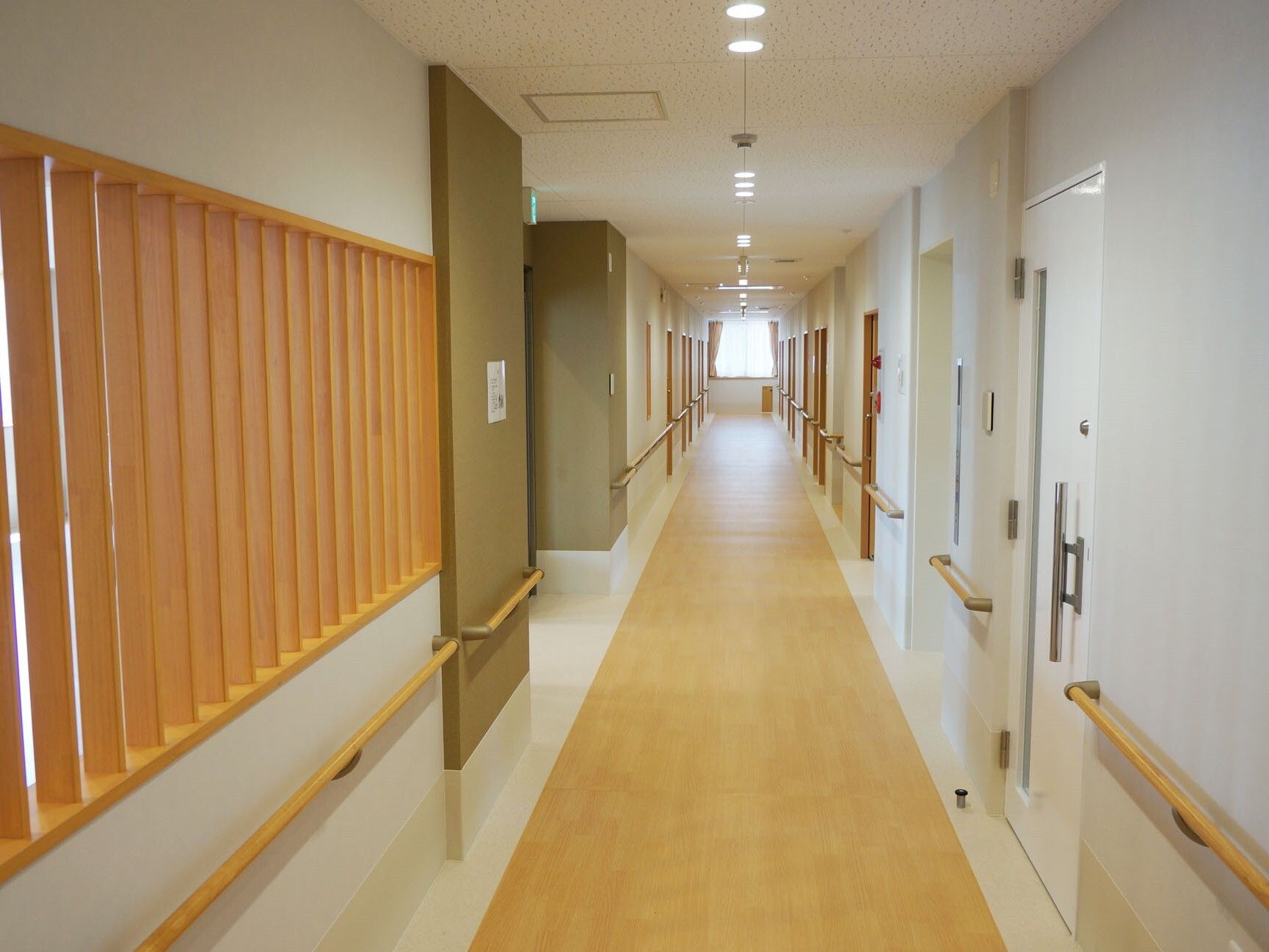廊下の中央は木目調で両サイドは壁と同じ白。壁には木目調の手すりが付き、居室のドアも廊下の両サイドに並んでいる。