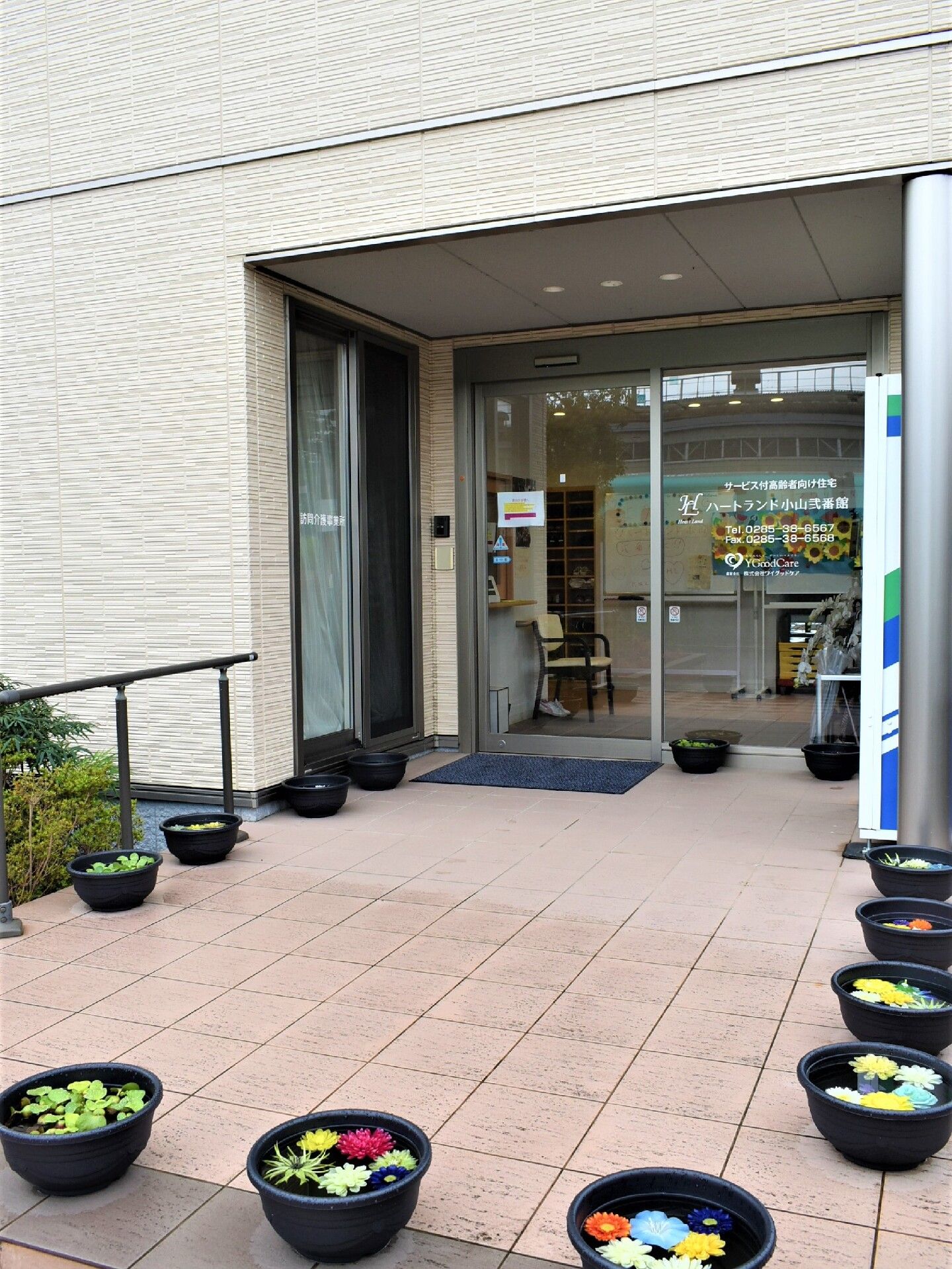 花が浮かべられている桶が玄関を囲むようにして置かれている。玄関には手すり付きのスロープもあり、自動ドアの前にはマットが敷かれている。