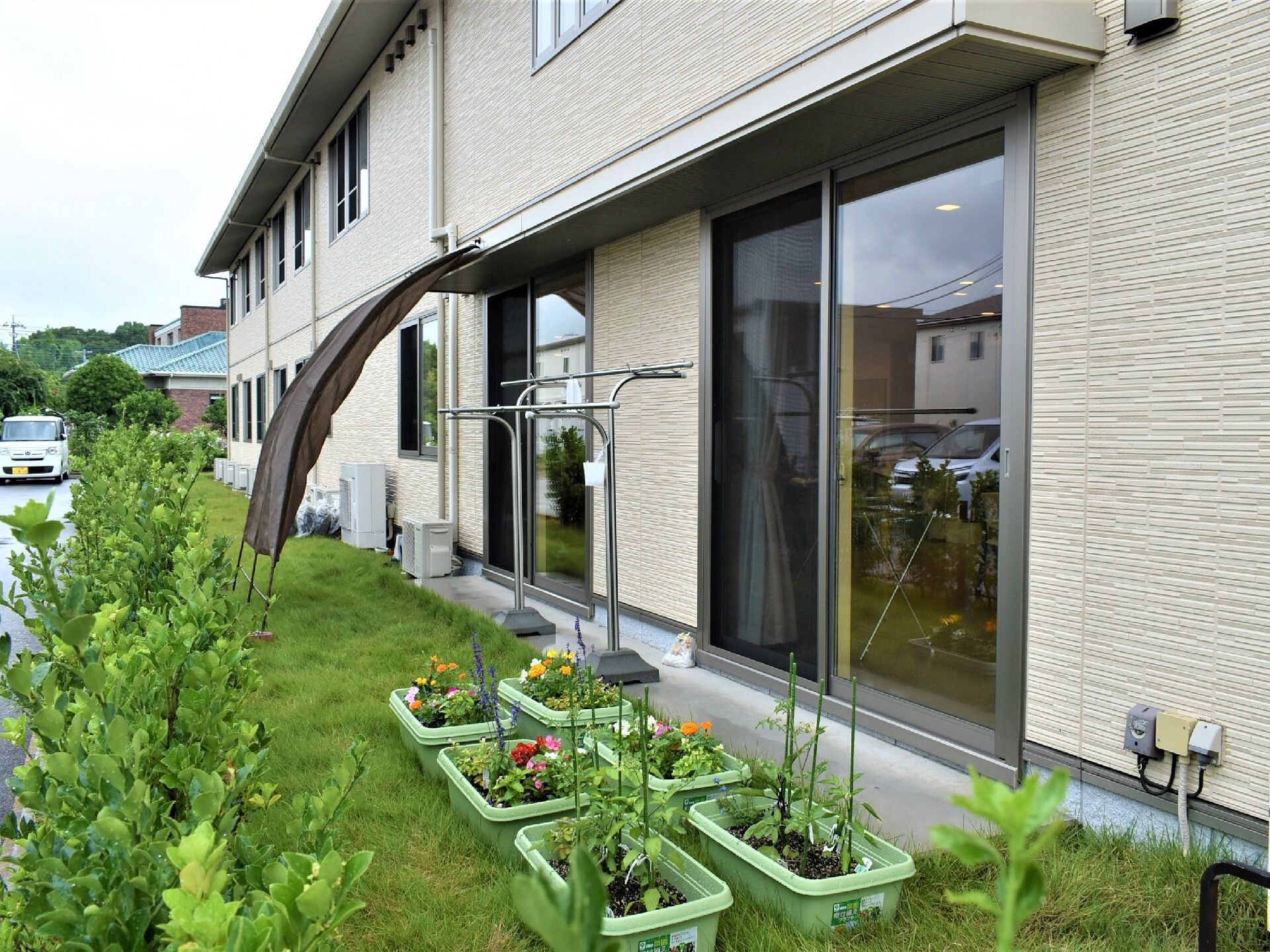食堂の大きな窓の外には野菜や花が植えられたプランターが置かれている。庭には芝生が植えられ、生垣も作られている。