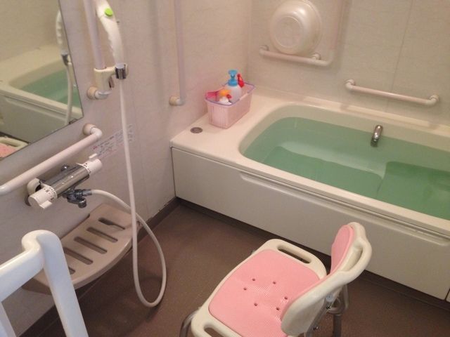 広い浴槽が設置された清潔感のある浴室である。洗い場には、シャワーや手すり、鏡や棚が取り付けられている。