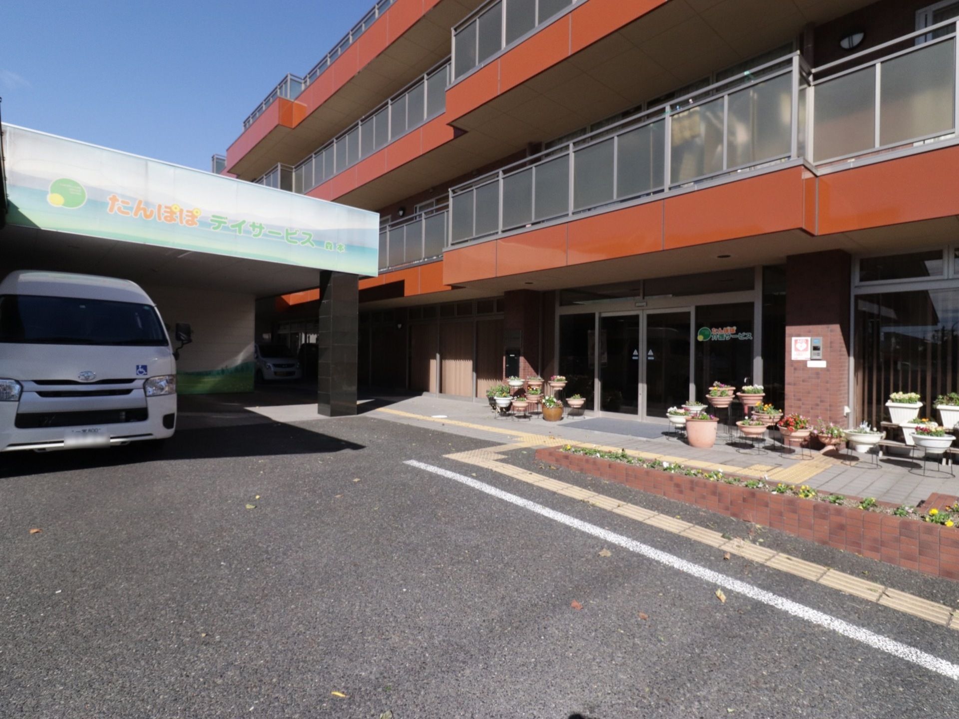 中央右側に自動ドアの玄関がある。その手前にはマットを敷いており、そばの通路には点字ブロックを設置している。