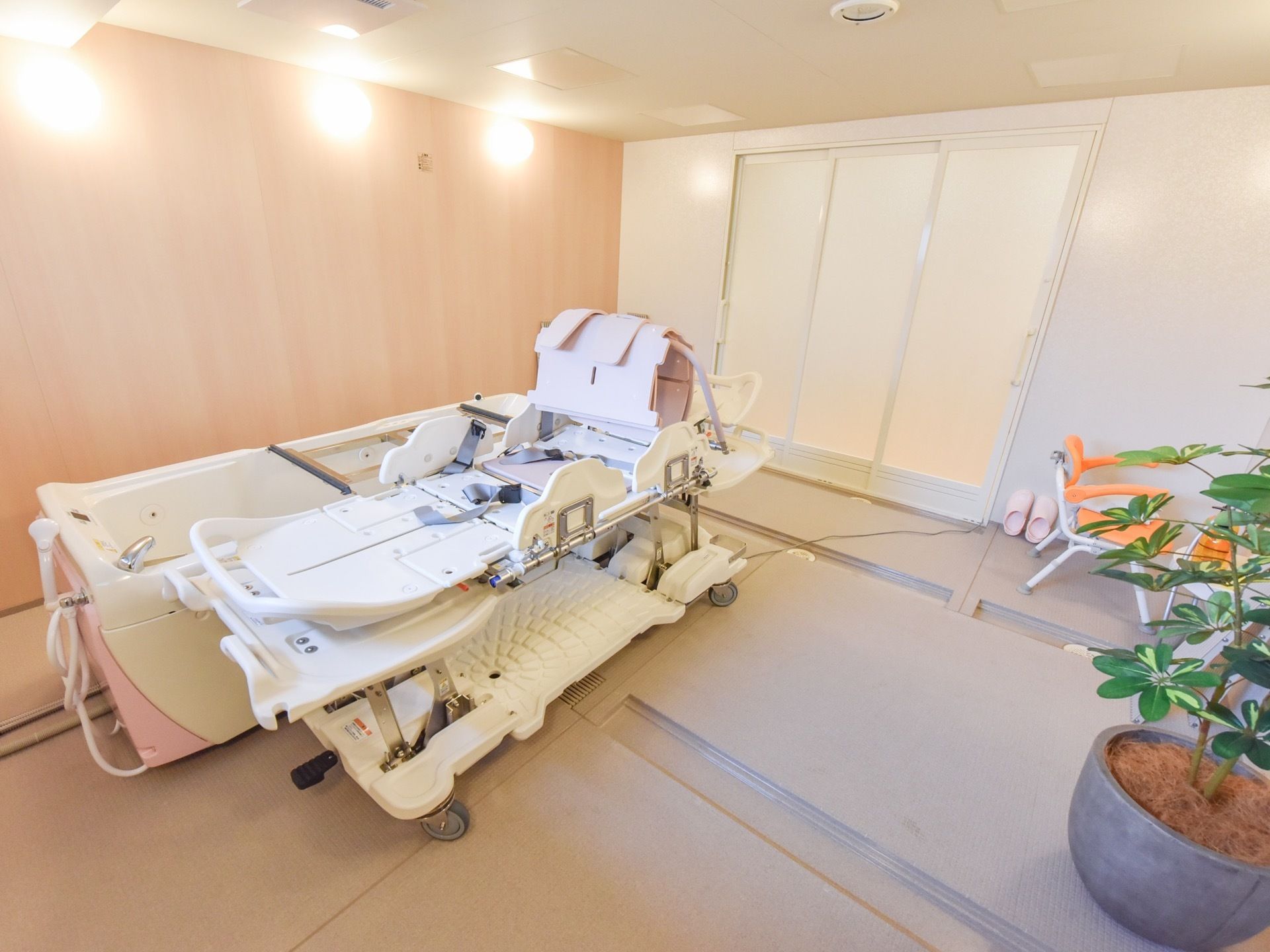 足腰に不安がある方のために、寝たままの姿勢で入浴できる器具が設置されている。緑が置かれており、あたたかみのある浴室である。