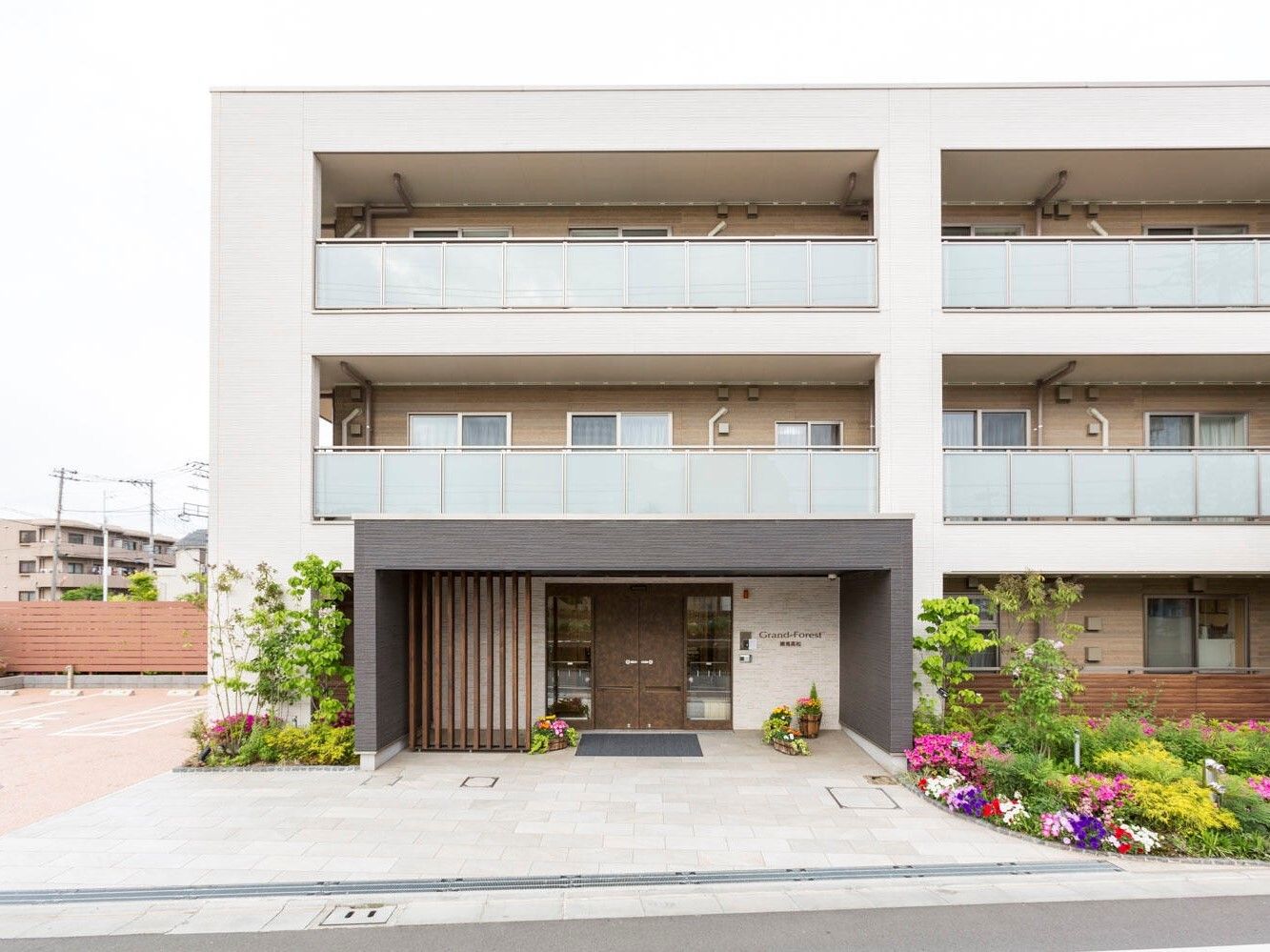庭に花壇があり玄関周りも緑に囲まれている三階建ての建物